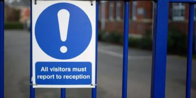 Blue school gate sign reading All visitors must report to reception highlighting the need for a visitor management system
